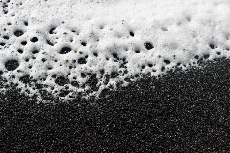 A black beach with white foam forming
