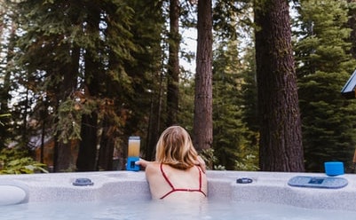 A woman relaxing in a hot tub with a smoothie with a forest background