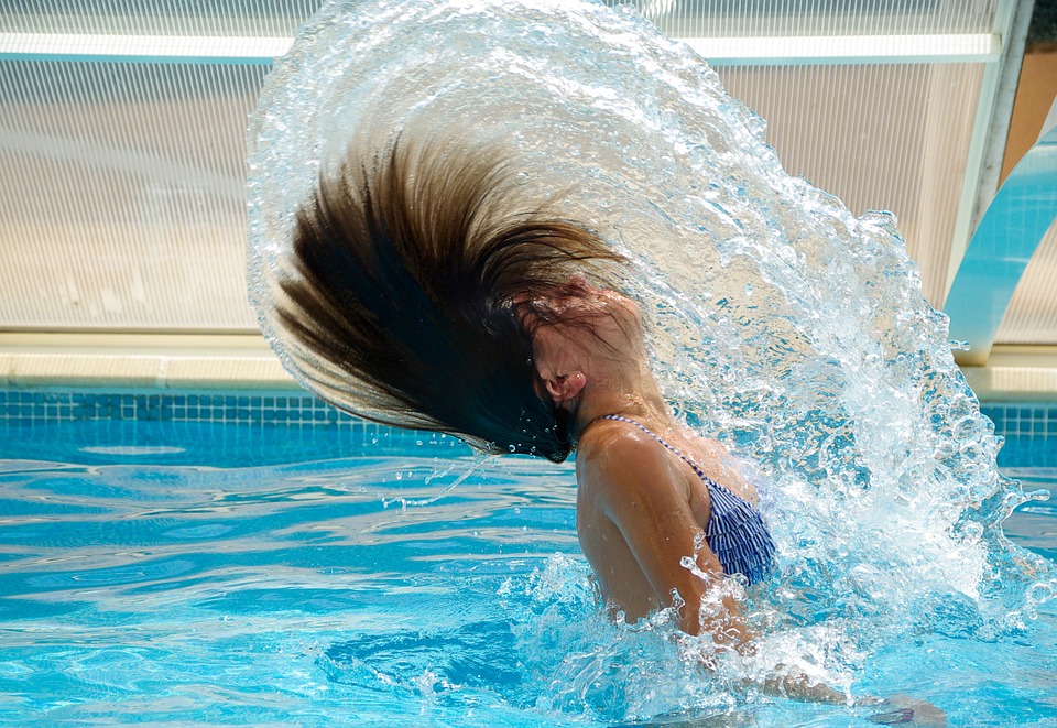 A woman in a swimming pool flinging her hair to create a water spiral effect