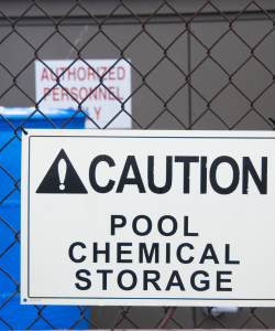 A warning sign on a fence that reads caution: pool chemical storage